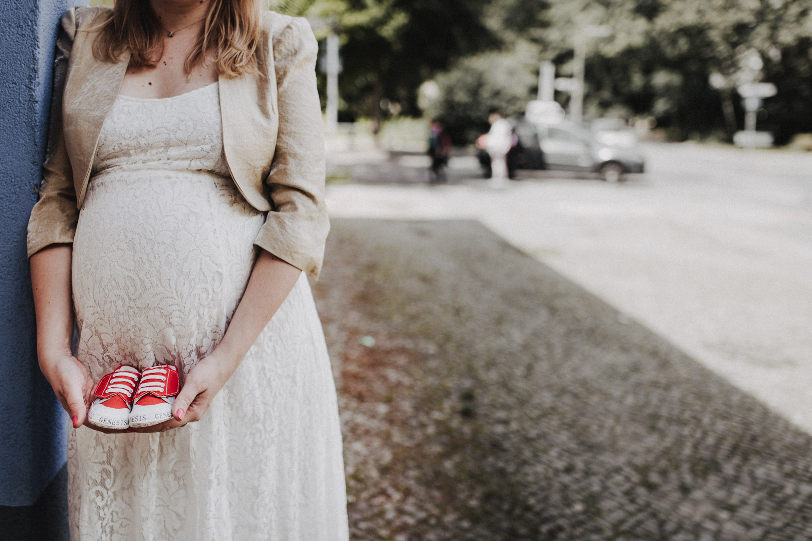 Familienfotograf Berlin: Werdende Mutter mit Babybauch und roten Babyschuhen an Wand gelehnt bei Schwangerschaftsfotos im Wedding
