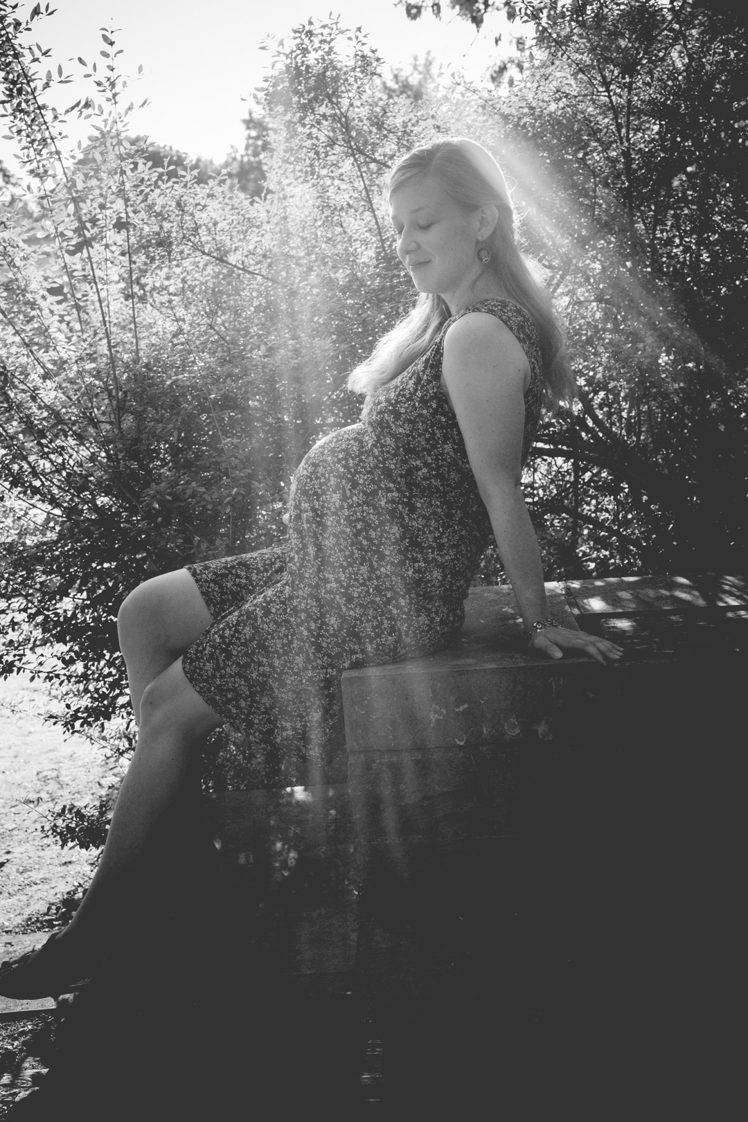 Familienfotograf Berlin Schwangerschaftsfotos: Babybauchfoto auf Insel der Jugend Berlin-Treptow. Werdende Mutter sitzt auf Stein im Gegenlicht