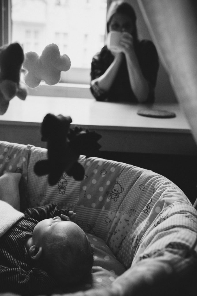 Neugeborenenfotos Berlin: Baby schaut zu Mobile über Stubenwagen bei Familienreportage in Berlin-Wedding