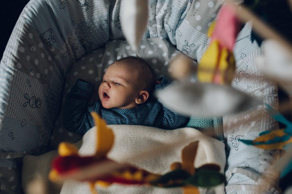 Neugeborenenfotos Berlin Familienreportage Berlin-Wedding: Baby liegt in Stubenwagen unter Mobile