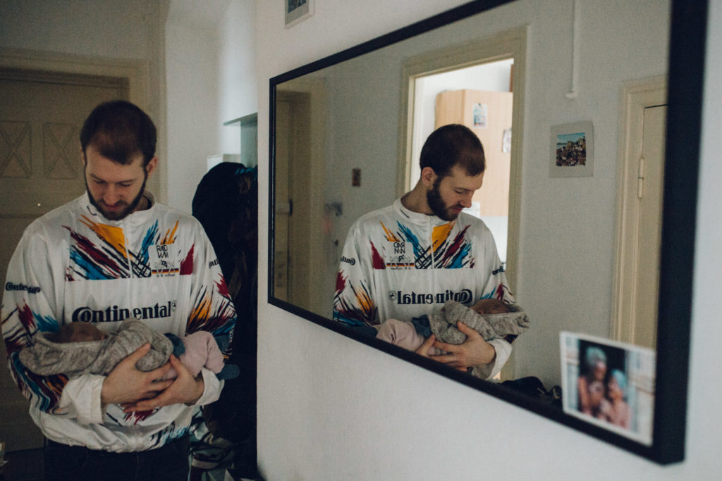Neugeborenenfotos Berlin: Vater trägt Neugeborenes im Arm vor Spiegel bei Familienreportage in Berlin-Wedding