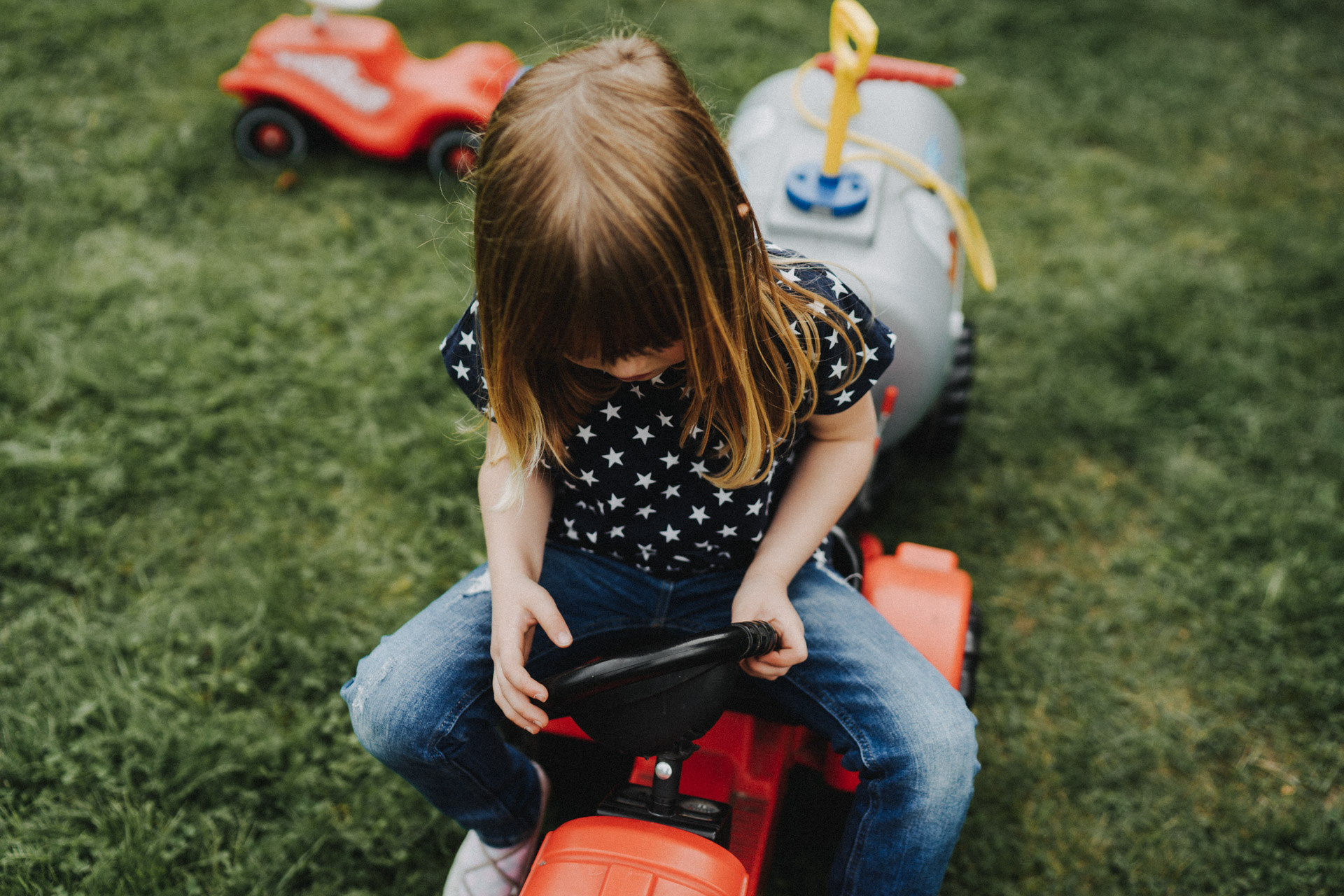 Familienreportage Berlin: Mädchen sitzt im Garten auf Spielzeugtraktor