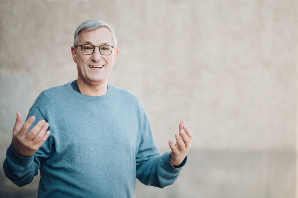 Portraits von Politikern Berlin: Parteivorsitzender Bernd Riexinger, gestikulierend in blauem Pullover vor grauer Wand