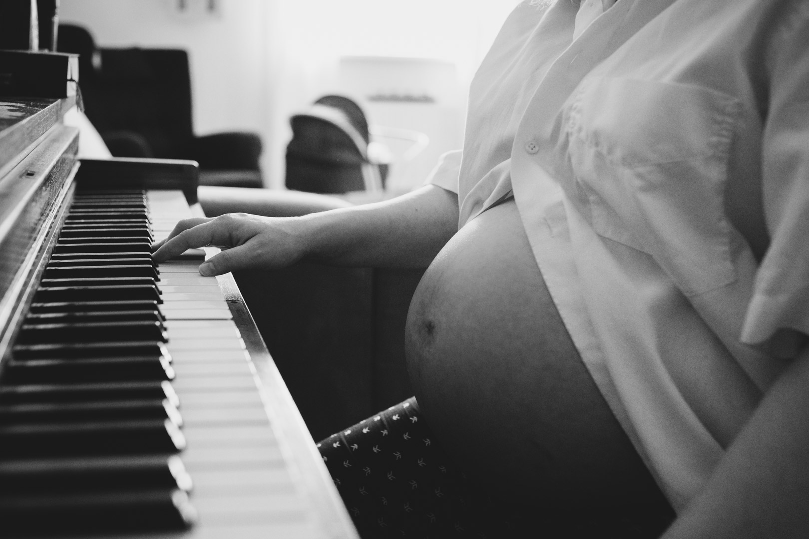 Familienfotograf Berlin Schwangerschaftsfotos: Schwarzweissfoto Babybauch an Klavier im Hintergrund steht ein Kinderwagen